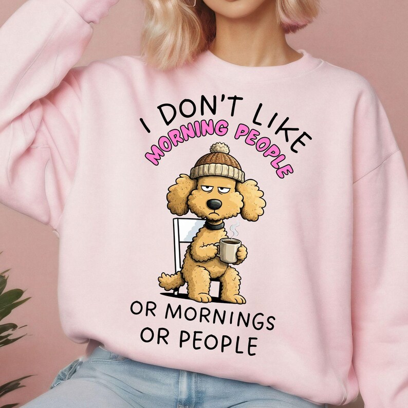 May include: Pale pink sweatshirt with the slogan "I DON'T LIKE MORNING PEOPLE OR MORNINGS OR PEOPLE." The design shows a cartoon dog in a beanie, holding a coffee cup, with a grumpy expression.