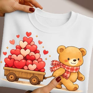 May include: White sweatshirt with a cartoon teddy bear pulling a cart of heart-shaped balloons. The bear wears a red and white plaid scarf. Red, pink, and white hearts and gold stars decorate the design. A lovely gift for Valentine's Day.