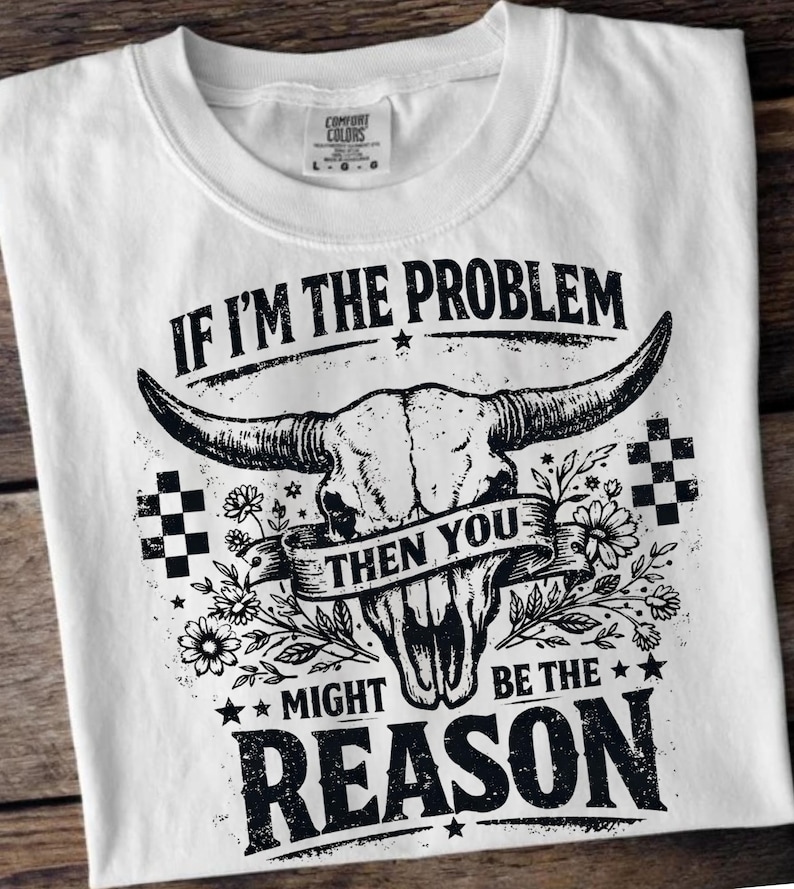 May include: White t-shirt with a graphic design featuring a bull skull, flowers, and the text "IF I'M THE PROBLEM THEN YOU MIGHT BE THE REASON." The shirt has a crew neck and short sleeves. The Comfort Colors tag is visible.