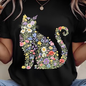 May include: Black t-shirt featuring a floral cat design. The cat silhouette is filled with colorful flowers in shades of yellow, white, blue, purple, and red. The design is centered on the front of the shirt.