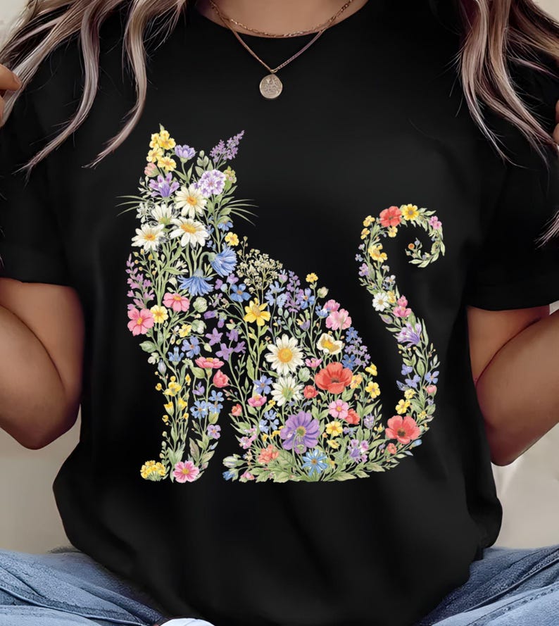 May include: Black t-shirt featuring a floral cat design. The cat silhouette is filled with colorful flowers in shades of yellow, white, blue, purple, and red. The design is centered on the front of the shirt.