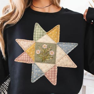 May include: Black sweatshirt featuring a large, colorful star design. The star is made of patchwork fabric in various pastel colors, with a floral embroidered center. The design gives a vintage, handcrafted aesthetic.