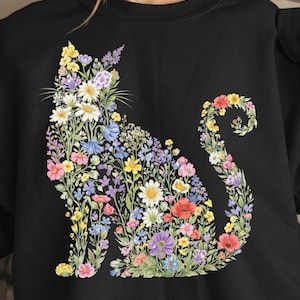 May include: Black sweatshirt featuring a floral cat design. The cat silhouette is composed of colorful flowers, including daisies, poppies, and lavender. The flowers are in shades of pink, yellow, blue, and purple.