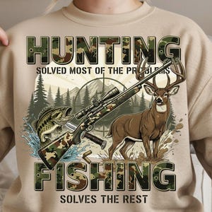 May include: Beige sweatshirt with a graphic featuring a deer, fish, and rifle. The text reads "HUNTING SOLVED MOST OF THE PROBLEMS FISHING SOLVES THE REST" in camouflage lettering. The design includes a mountain and forest backdrop.