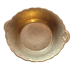 May include: A gold-colored serving bowl with a floral pattern and two handles. The bowl is made of glass and has a scalloped edge.