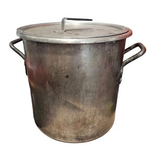 May include: A large, silver, aluminium stock pot with two handles and a lid. The pot has a worn, used appearance.