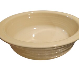 May include: A cream-colored ceramic bowl with a wide rim and a slightly textured exterior. The bowl has a smooth, glossy interior and is designed for serving food. The bowl is a neutral color and can be used for various purposes.