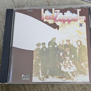 以下が含まれることがあります： 透明なプラスチックケースに入ったLed Zeppelin IIの音楽CD。カバーには、茶色と白の背景に軍服を着た人々のグループのセピア調の写真が写っており、Led Zeppelin IIとAtlanticの文字が記載されています。