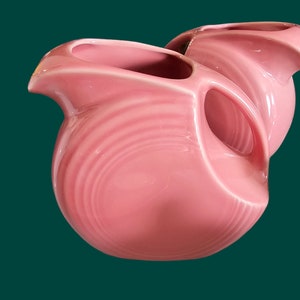 May include: Two pink ceramic pitchers with a ridged design. The pitchers are made in a rounded shape with a wide opening and a handle.