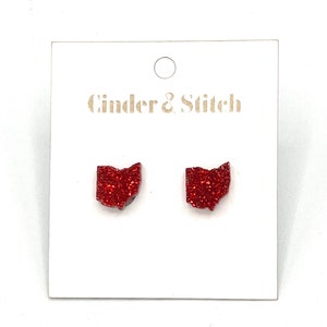 May include: A pair of red glitter Ohio state earrings on a white card with the text "Cinder & Stitch".