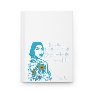 Peut inclure: Journal blanc avec une illustration bleue d'une femme avec un motif floral et des tournesols. Le journal comprend le texte "It is a blessing to be the color of earth. Do you know her then? Flowers confuse us for home. Rupi Kaur."