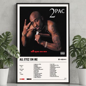 May include: A framed poster featuring 2Pac, with the text "2PAC" at the top. The poster includes the album title "All Eyez On Me" and a tracklist. The image shows 2Pac with jewelry and tattoos, set against a black background.