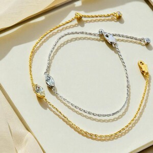 Puede incluir: Dos pulseras finas, una dorada y otra plateada. Cada una presenta una piedra preciosa central con forma de marquesa. La pulsera dorada tiene una peque&ntilde;a gema redonda en el cierre. La pulsera plateada tiene una gema similar en el cierre.