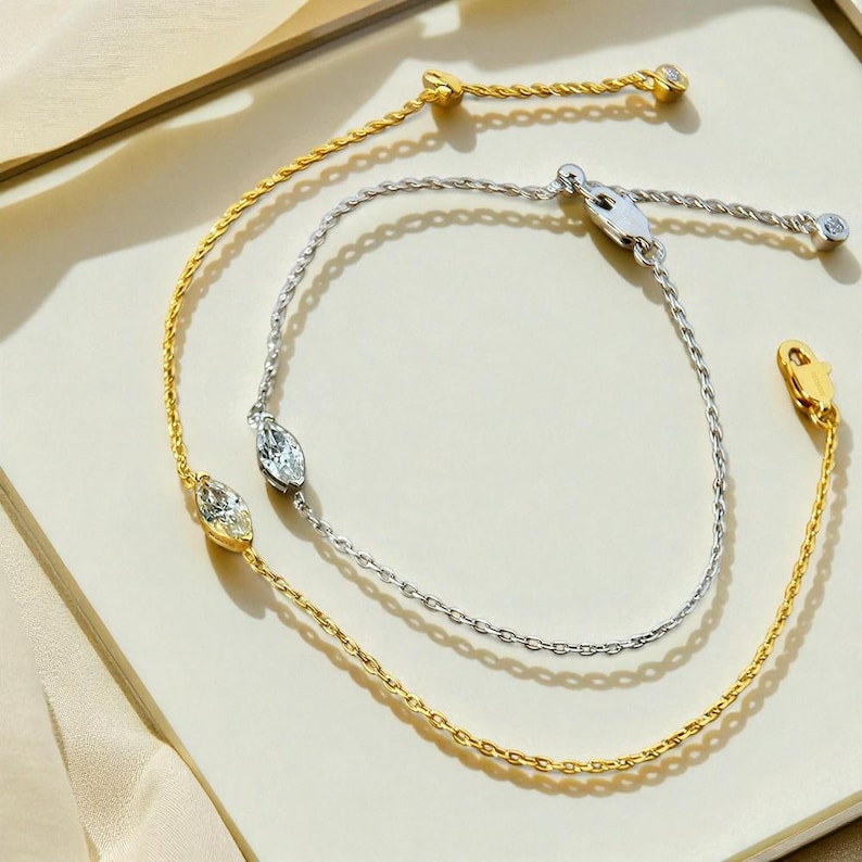 Puede incluir: Dos pulseras finas, una dorada y otra plateada. Cada una presenta una piedra preciosa central con forma de marquesa. La pulsera dorada tiene una peque&ntilde;a gema redonda en el cierre. La pulsera plateada tiene una gema similar en el cierre.