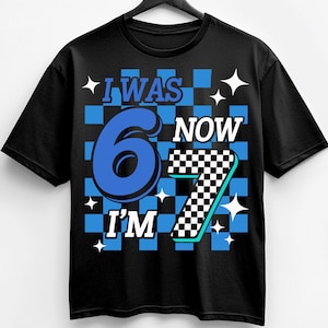 Pu&ograve; includere: T-shirt nero con la scritta "I WAS 6 NOW I'M 7". Il design presenta uno sfondo a scacchi blu e bianco con il numero 6 in blu e il numero 7 in un motivo a scacchi bianco e nero.