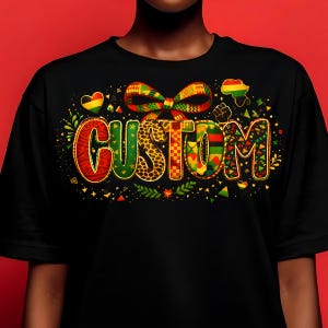 Op de afbeelding: Zwart T-shirt met het woord "CUSTOM" in een kleurrijk, patroonontwerp. Het ontwerp bevat een strik, harten, een omtrek van Afrika en een vuist. De letters zijn gevuld met verschillende patronen, waaronder luipaardprint en geometrische vormen.