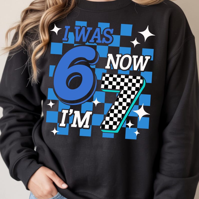Pu&ograve; includere: Felpa nera con un motivo a scacchi blu e bianchi. Il testo recita "I WAS 6 NOW I'M 7" in blu e bianco. Grafiche a forma di stella bianca sono sparse intorno al testo. Una divertente maglietta di compleanno.