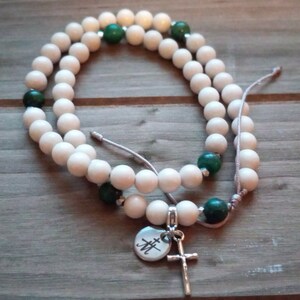 May include: White and green beaded bracelet with a silver charm featuring a cross and the initials "JH".