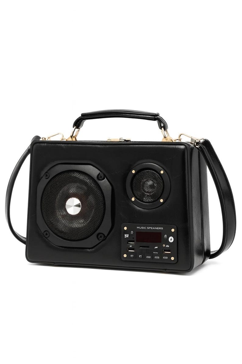 Puede incluir: Bolso de mano negro de cuero sint&eacute;tico dise&ntilde;ado para parecerse a un boombox vintage. Cuenta con un altavoz grande, un altavoz m&aacute;s peque&ntilde;o y una pantalla digital. El bolso tiene un asa superior y una correa para el hombro. El texto "MUSIC SPEAKERS" es visible.