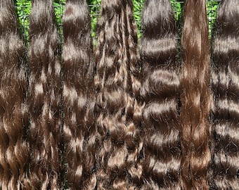 以下が含まれることがあります： 緑色のメッシュの背景に、7つの束の波状の濃い茶色のヘアエクステンションが表示されています。髪は上部を黒い糸または赤いリボンで結んでいます。髪の色と質感が異なり、束によっては明るい茶色の色合いになっています。