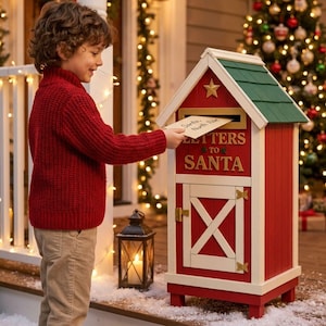 Könnte beinhalten: Ein rot-weißer Briefkasten aus Holz in Scheunenform mit grünem Dach und der Aufschrift Letters to Santa in Gold. Eine Hand steckt einen Umschlag mit der Aufschrift Santa North Pole in den Schlitz. Der Briefkasten hat eine Tür mit einem weißen X.
