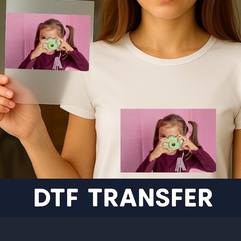 May include: White t-shirt featuring a printed image of a girl with a green camera. A clear transfer sheet with the same image is held in front of the shirt. The words "DTF TRANSFER" are printed in white on a dark blue background.