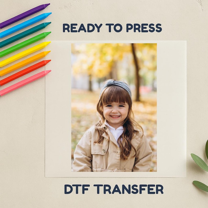 May include: A print-ready DTF transfer featuring a smiling child wearing a headband and tan jacket. The image is on a cream-coloured background, with colourful crayons in the upper left corner. Text at the top reads "READY TO PRESS" and "DTF TRANSFER" at the bottom.