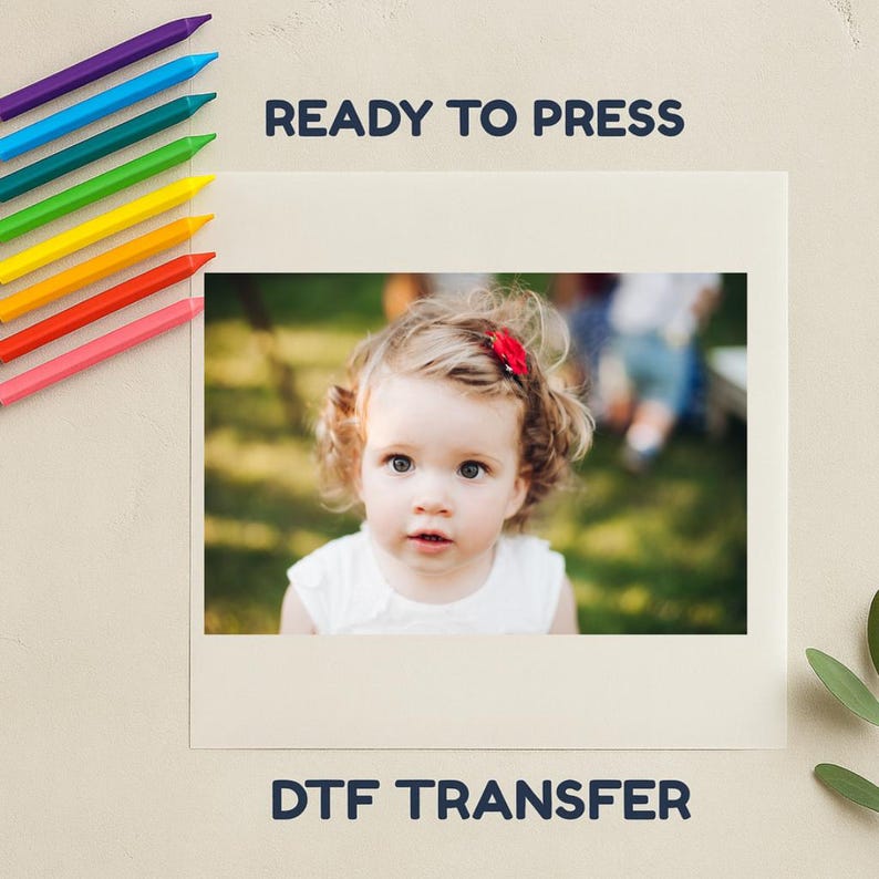 May include: A cream-coloured print featuring a photograph of a young child with curly hair and a red hair accessory. The text "READY TO PRESS" and "DTF TRANSFER" are printed in navy blue.