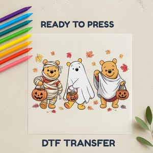 May include: DTF transfer featuring three Winnie the Pooh characters in Halloween costumes. One is wrapped in bandages, another is a ghost, and the third is in a sheet. Each holds a jack-o'-lantern bucket. The words "READY TO PRESS" and "DTF TRANSFER" are printed on the image.