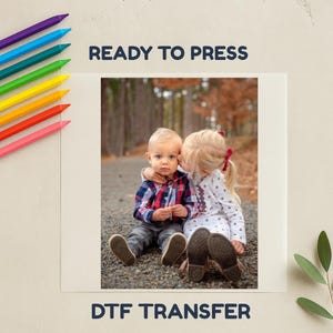 May include: A DTF transfer with a photograph of two children, one kissing the other. The image is framed by the text "READY TO PRESS" and "DTF TRANSFER". Colour pencils are in the upper left corner.