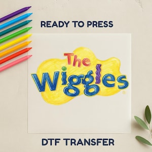May include: A DTF transfer featuring "The Wiggles" logo in blue, yellow, and red. The text "READY TO PRESS" and "DTF TRANSFER" are displayed. Rainbow-coloured pencils are arranged along the left side.
