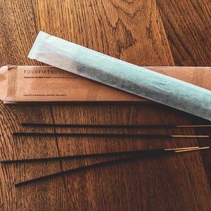 May include: A package of charcoal incense sticks with the text "FOURFIFTYONE" on the box. The box is brown, and the incense sticks are black with gold tips. The incense is wrapped in a light blue paper.