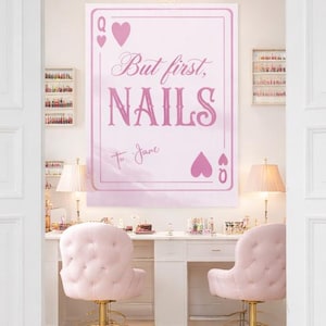 Puede incluir: Interior de un salón de manicura rosa claro y blanco, con un letrero que dice "But first, NAILS". La habitación cuenta con sillas rosas, un escritorio blanco y una lámpara de araña. Las paredes son blancas y los pisos de madera clara.