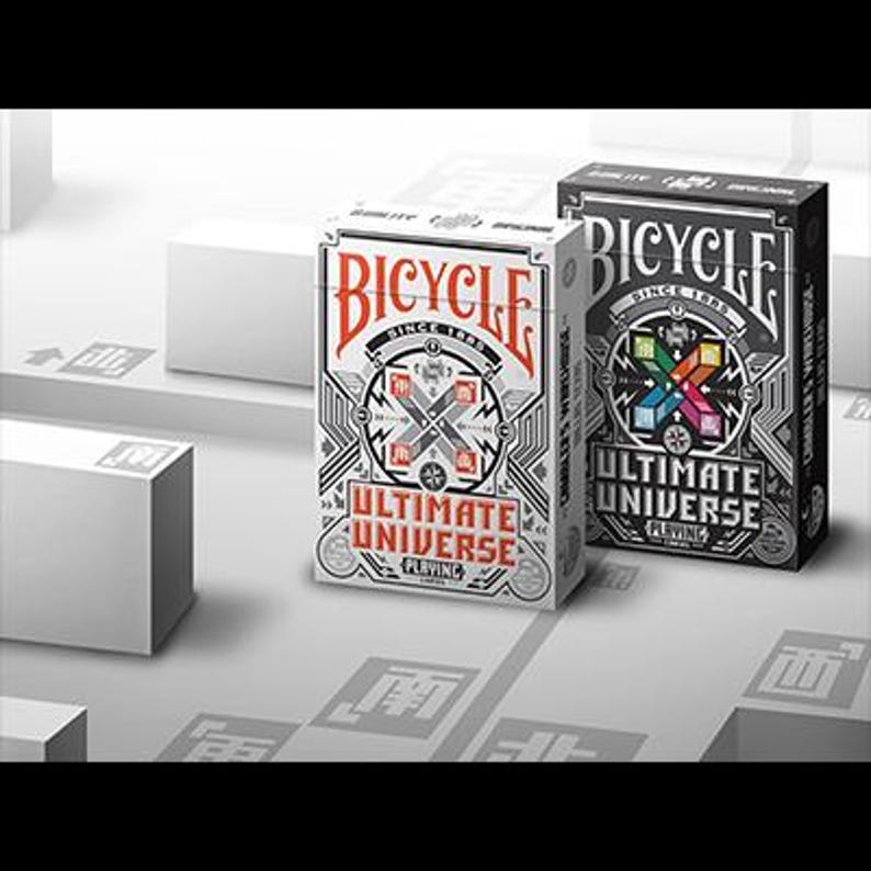 Puede incluir: Dos barajas de cartas Bicycle, una blanca y otra negra, con "Ultimate Universe" impreso en las cajas. La baraja blanca presenta detalles en rojo y negro, mientras que la baraja negra tiene un dise&ntilde;o colorido. El logotipo de Bicycle es prominente.
