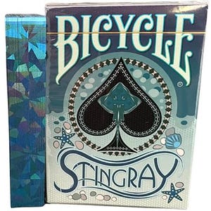 May include: A Bicycle playing card deck with a blue and white design, featuring a stingray illustration within a spade symbol. The box has the word "Bicycle" at the top and "Stingray" at the bottom. A blue, iridescent card sleeve is next to the deck.