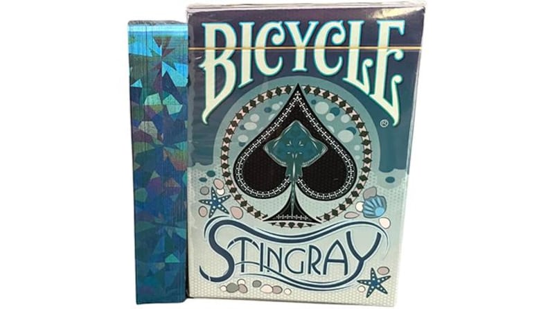 May include: A Bicycle playing card deck with a blue and white design, featuring a stingray illustration within a spade symbol. The box has the word "Bicycle" at the top and "Stingray" at the bottom. A blue, iridescent card sleeve is next to the deck.