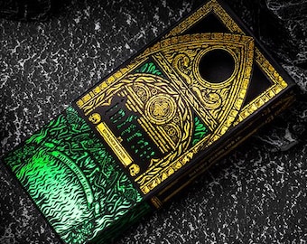 May include: A deck of cards with a black and gold design, featuring intricate patterns and the words "ENTRANCE EDITION". The cards have a green, textured design on the side. The deck is set against a dark, textured background.