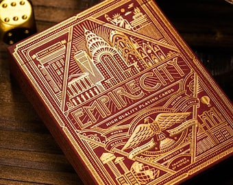 May include: A deck of Empire City playing cards with a burgundy background and gold embossed details. The design features cityscapes, an eagle, and the text "Empire City" and "High Quality Playing Cards". Two gold dice are in the background.