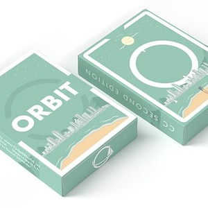 May include: Two mint green Orbit Second Edition playing card decks. The boxes feature a white border, the word "ORBIT" in large white letters, and a cityscape design. The second box has a large white circle and the text "CC SECOND EDITION".