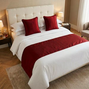 Può includere: Un letto con copriletto bianco, due cuscini rossi e un runner da letto rosso. La testiera è beige chiaro. La stanza è in una combinazione di colori neutri.