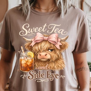 May include: A brown t-shirt featuring a cartoon Highland cow wearing a pink bow, with the text "Sweet Tea and Side Eye." A glass of iced tea with a lemon slice and straw is also depicted.