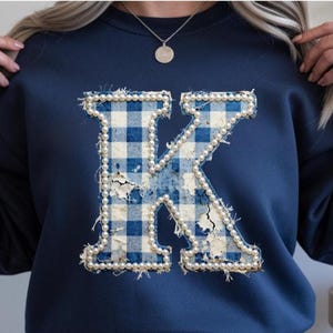 May include: Navy blue sweatshirt featuring a large letter "K" applique. The letter is made of blue and white gingham fabric, embellished with faux pearls around the edges. The applique has a distressed, vintage look.