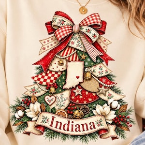 May include: A cream-colored sweatshirt featuring a graphic of a Christmas tree composed of patterned ribbons, ornaments, and a map of Indiana with a small red heart. The design includes a large red bow at the top and a banner at the base reading Indiana.