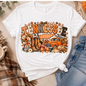 Może przedstawiać: Biały t-shirt z kr&oacute;tkim rękawem z nadrukiem graficznym słowa TENNESSEE w pomarańczowe i czarne wzory. Projekt zawiera pomarańczową ciężar&oacute;wkę, kowbojki, gitarę, piłkę do futbolu amerykańskiego, kapelusz, słoneczniki i pomarańczowe kokardy w kratę.