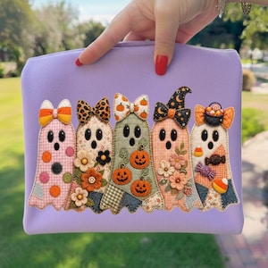 May include: A light purple zippered pouch featuring an applique design of five ghosts. Each ghost has a unique pattern, including gingham, floral, and polka dots, and is decorated with bows, pumpkins, flowers, and candy corn motifs.