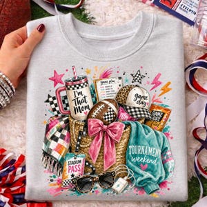May include: A light gray sweatshirt featuring a graphic print of a straw basket filled with a tumbler labeled "I'm That Mom," a football, a baseball cap labeled "game day," a "stadium pass," sunglasses, and a teal shirt labeled "tournament weekend."