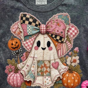 Puede incluir: Una camiseta gris Comfort Colors con un diseño caprichoso de fantasma de Halloween. El fantasma tiene un lazo de retazos, una cara sonriente y está rodeado de calabazas y flores. El diseño incorpora acentos rosas, naranjas y negros.