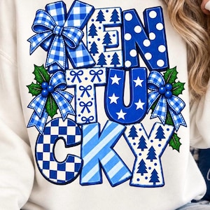 May include: A white sweatshirt featuring the word KENTUCKY in large, blocky letters. Each letter has a unique blue and white pattern, including gingham bows, pine trees, polka dots, stars, stripes, and holly leaves with blue berries.