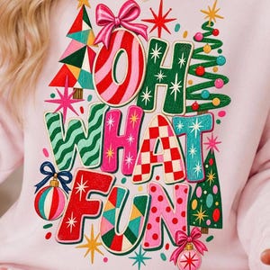 K&ouml;nnte beinhalten: Ein hellrosa Sweatshirt mit einer bunten Grafik und dem Schriftzug "OH WHAT FUN" in verschiedenen Mustern und Farben. Das Design zeigt stilisierte Weihnachtsb&auml;ume, Christbaumkugeln mit Schleifen und Sternmotive in Rot, Gr&uuml;n, Pink und T&uuml;rkis.
