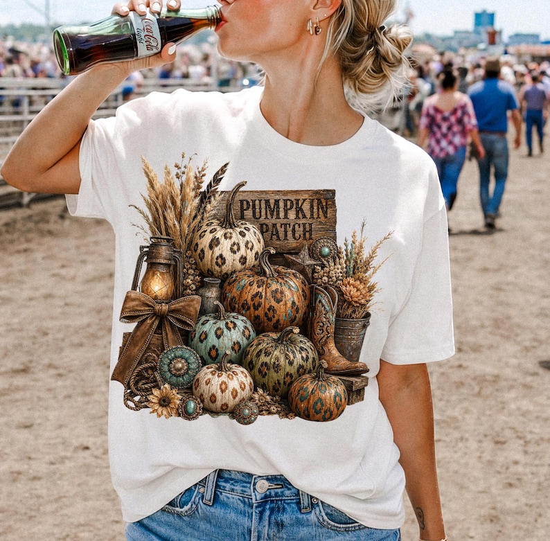 May include: White t-shirt featuring a fall-themed graphic with pumpkins, a lantern, and the text "PUMPKIN PATCH". The design includes various pumpkins, wheat, and a pair of cowboy boots, evoking a rustic autumn aesthetic.